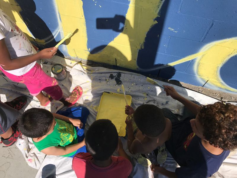 Photo of youth helping paint a community wall.