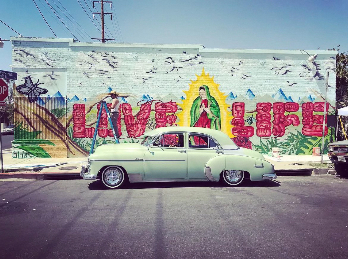 Image of a mural being painted with text that reads \x22Love Life,\x22 and a painting of the virgen de guadalupe.